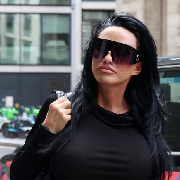 Katie Price mit langen schwarzen Haaren und großer Sonnenbrille trägt schwarzes Oberteil und steht auf einer Straße vor einem Auto.