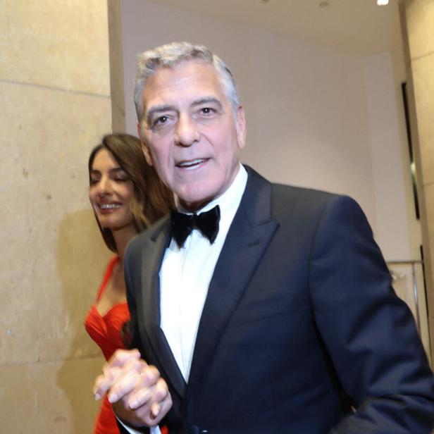 George Clooney im Smoking mit Amal Clooney in rotem Kleid.