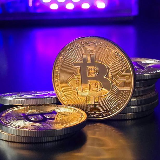 Bitcoin und Münzen liegen auf einem Tisch, beleuchtet von einem lila Licht.