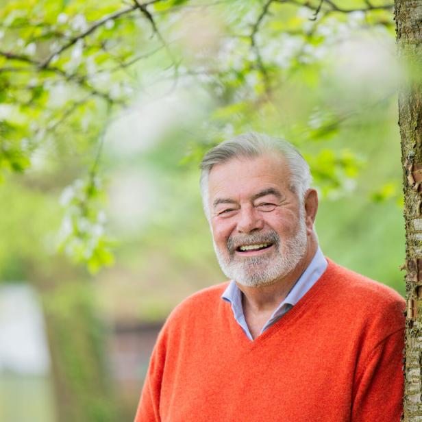 Ein lächelnder Harry Wijnvoord mit Bart lehnt an einem Baum im Grünen.