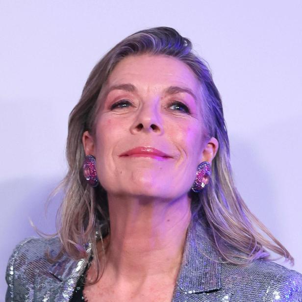 Caroline von Monaco mit blondem Haar trägt einen glitzernden Blazer und auffällige Ohrringe.
