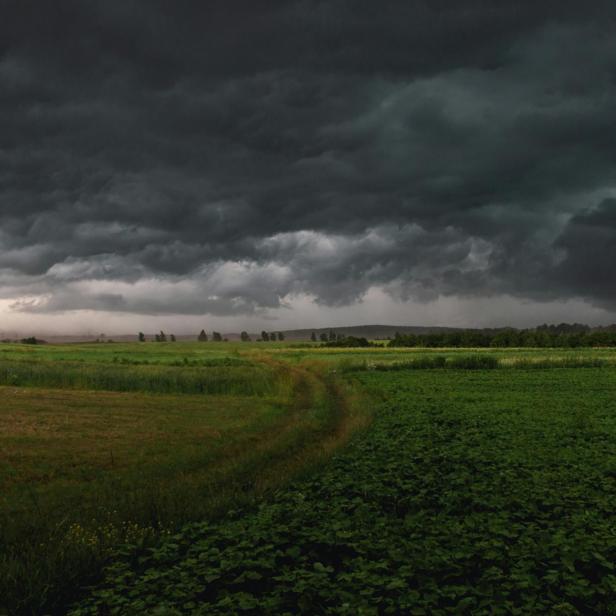 Dunkle Gewitterwolken ziehen über eine grüne Landschaft mit Feldern und Wiesen.