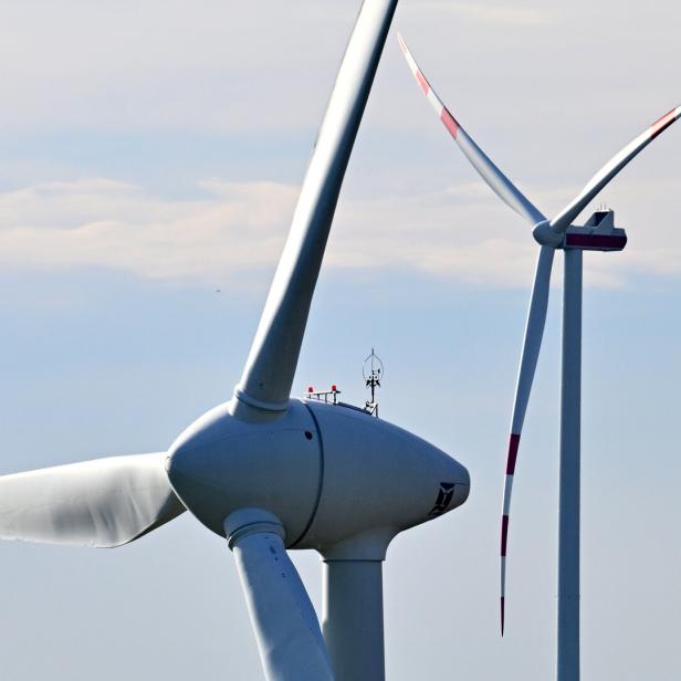 Zwei Windräder mit rot markierten Spitzen stehen vor einem hellen Himmel.