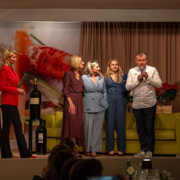 Fünf Personen stehen auf einer Bühne vor einem großen Essensmotiv, während eine Person ins Mikrofon spricht.