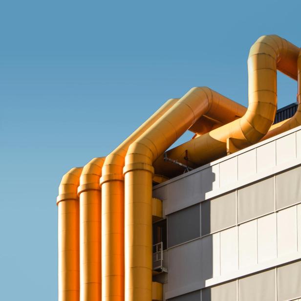 Gelbe Industrie-Rohre verlaufen an der Fassade eines modernen Gebäudes vor blauem Himmel.