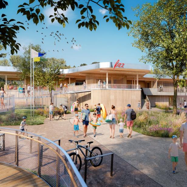 Viele Menschen in Sommerkleidung gehen mit Schwimmutensilien zu einem modernen Freizeitbad mit Holzfassade und grüner Umgebung.