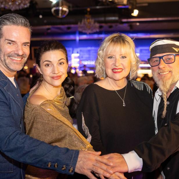 Vier lächelnde Personen legen ihre Hände übereinander in einem festlichen Rahmen.