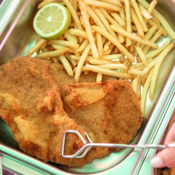 In einer Metallschale liegen Schnitzel, Pommes und eine Zitronenscheibe.