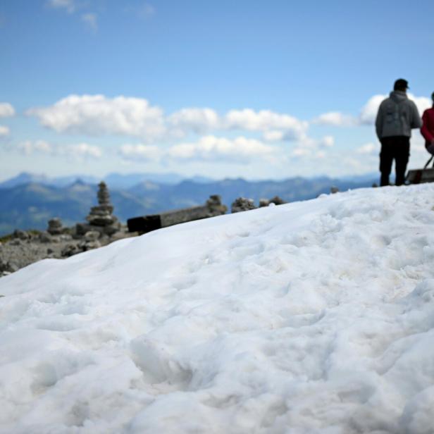 Zwei Personen stehen auf einer verschneiten Bergkuppe mit Steinmännchen und Blick auf eine Berglandschaft.