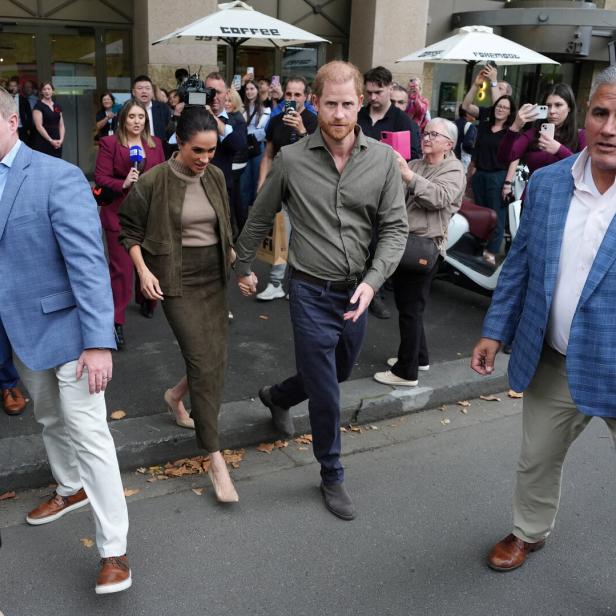 Harry und Meghan gehen Händchen haltend durch eine Menschenmenge.