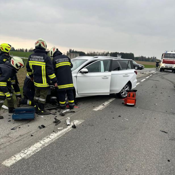 Feuerwehr-Helfer vor einem weißen Unfallwrack