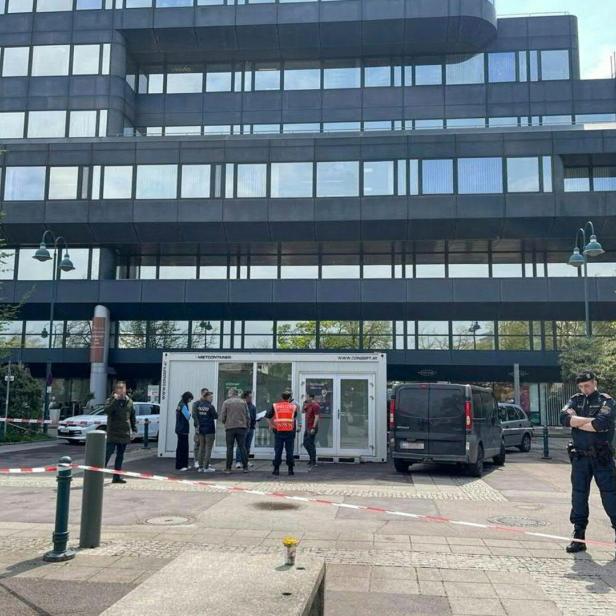 Mehrere Polizisten und Personen stehen vor einem abgesperrten Bereich vor einem modernen Bürogebäude.