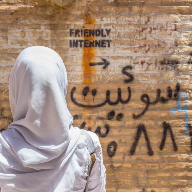 Veiled woman watching inscription on wall indicating uncensored Internet spot