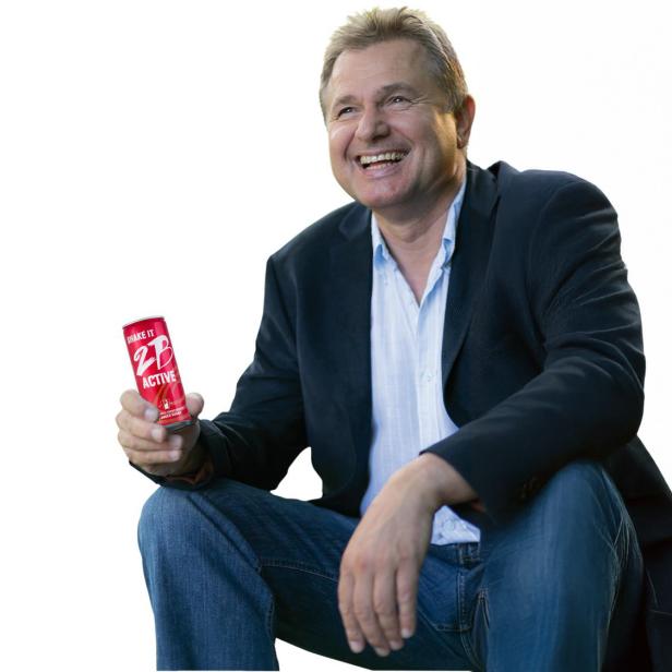 Ein Mann sitzt und hält lächelnd eine Getränkedose in der Hand.