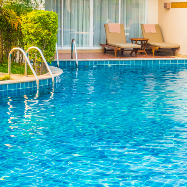 Ein Schwimmbad mit Liegen, umgeben von Palmen und Sonnenschein.