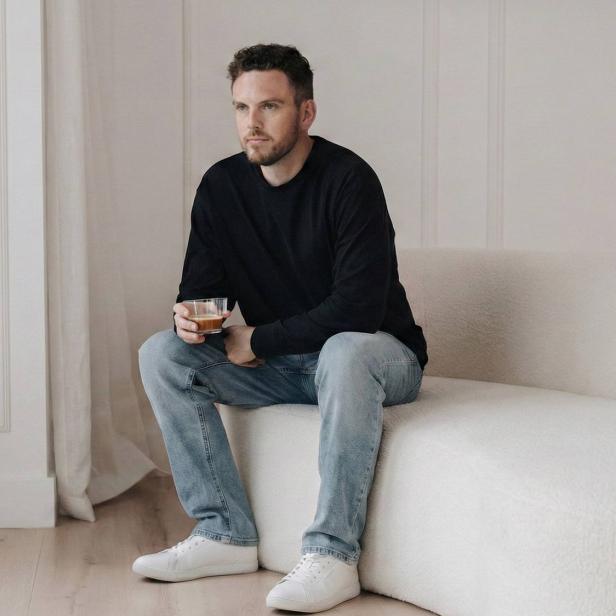 Ein Mann sitzt auf einer Couch mit einer Tasse Kaffee in der Hand.