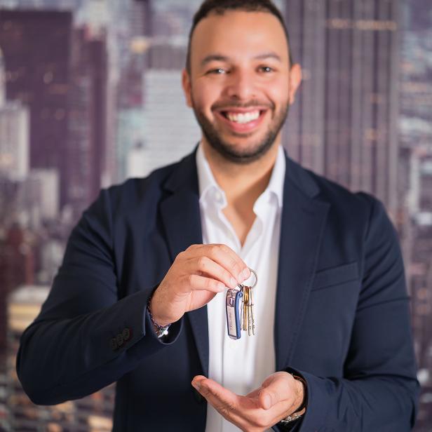 Ein Mann hält einen Schlüssel vor einer Stadtlandschaft in der Dämmerung.