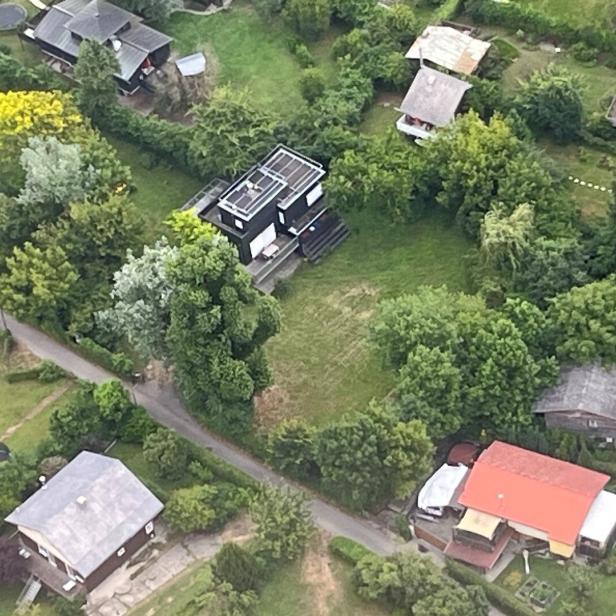 Luftaufnahme von Wohnhäusern mit Gärten und Bäumen in einer grünen Landschaft.