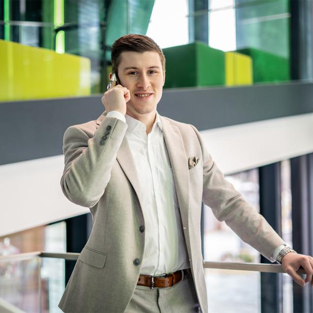 Junger Mann im Anzug telefoniert in einem modernen, lichtdurchfluteten Bürogebäude.