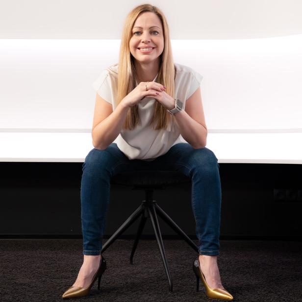 Eine Frau sitzt auf einem Stuhl vor einer weißen Wand.