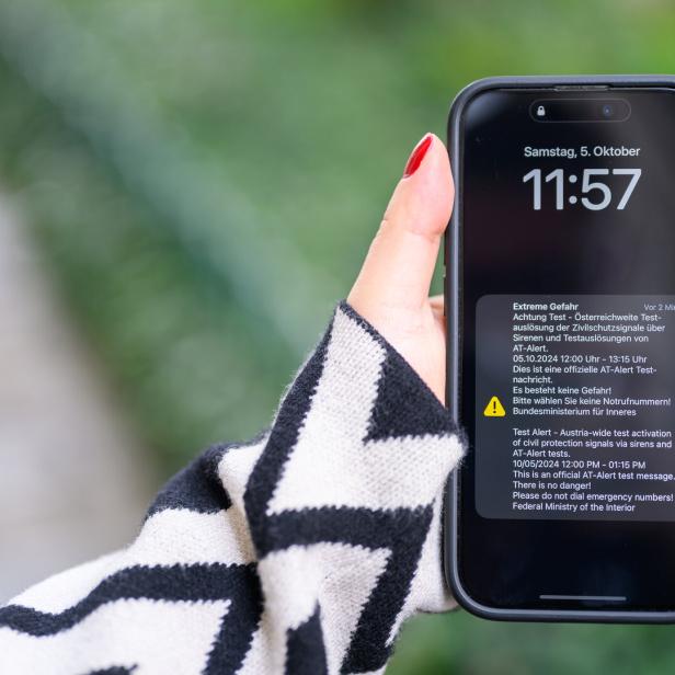 Eine Hand hält ein Smartphone, das eine Warnmeldung des Bundesministeriums für Inneres anzeigt.