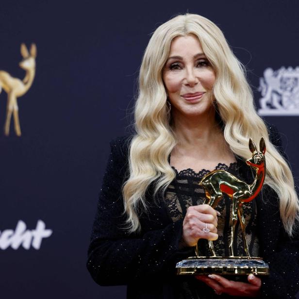 Cher hält eine goldene Bambi-Trophäe vor einem dunklen Hintergrund.