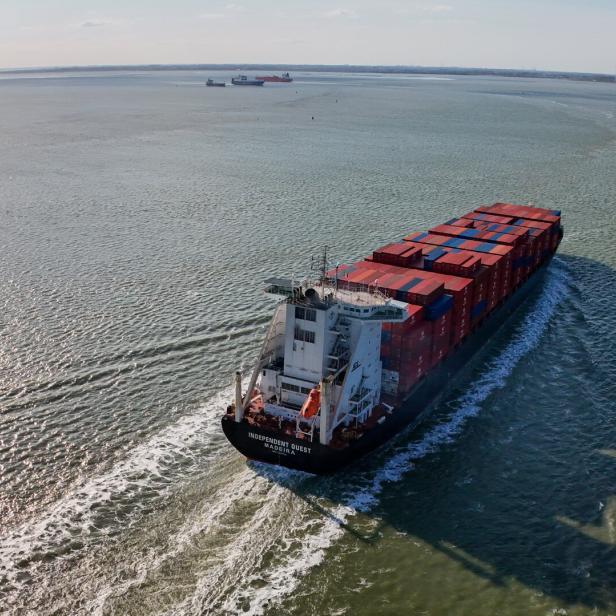 Ein großes Containerschiff fährt auf dem Meer, beladen mit vielen roten und blauen Containern.