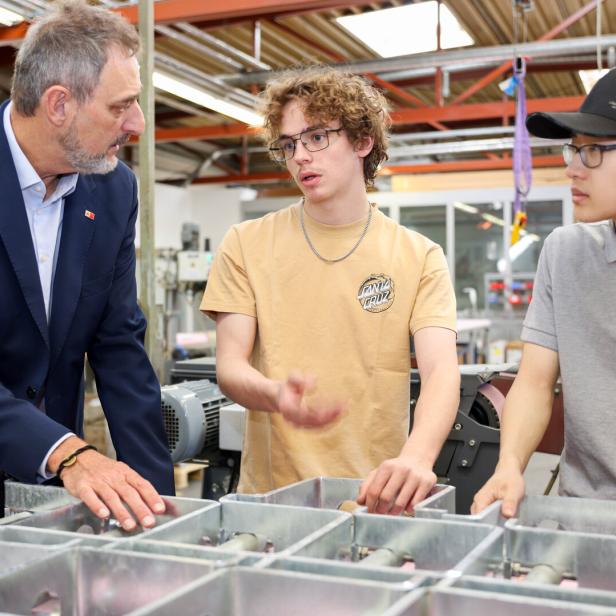 Drei Männer unterhalten sich in einer Werkstatt an einer Metallkonstruktion.