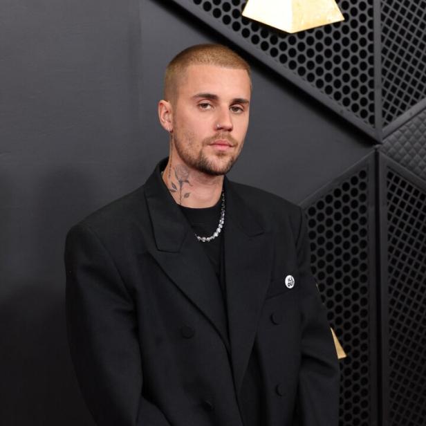 Justin Bieber trägt einen schwarzen Blazer und eine silberne Halskette vor einem dunklen Hintergrund.