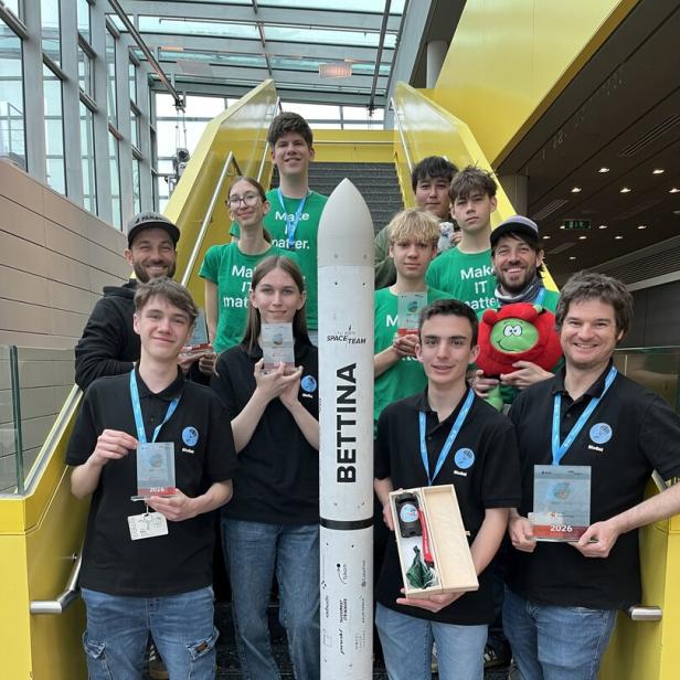 Eine Gruppe junger Menschen steht auf einer Treppe um eine Modellrakete und hält Auszeichnungen in den Händen.