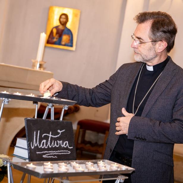 Ein Geistlicher zündet in einer Kirche eine Kerze an, im Hintergrund ein Ikonenbild und eine Tafel mit der Aufschrift „Matura“.