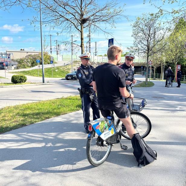 Ein Radfahrer wird von zwei Polizisten auf einem Weg angehalten.