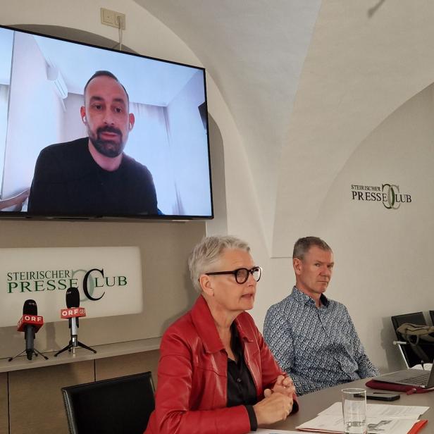 Mann und Frau an Tisch, im Hintergrund Bildschirm mit Bild eines Mannes