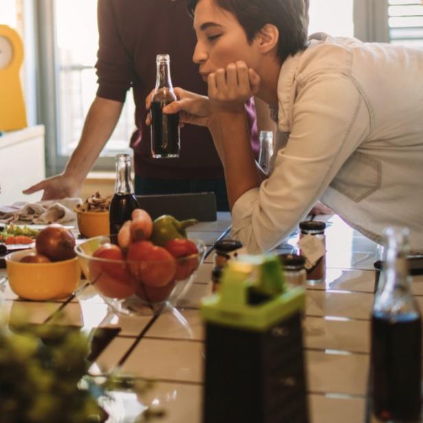 Drei junge Menschen unterhalten sich in einer Küche mit Obst und Getränken auf dem Tisch.
