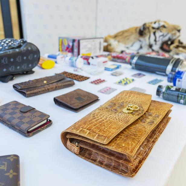 Auf einem Tisch liegen diverse Geldbörsen, Pillen, ein Tigerfell und andere Gegenstände.