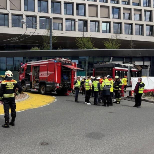 Einsatzkräfte der Berufsfeuerwehr Salzburg und Rettungsdienste am Unfallort mit einer beschädigten Straßenbahn.