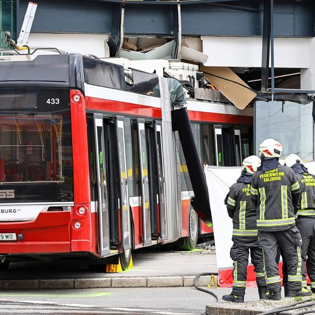 Ein roter Bus ist in ein Gebäude gefahren, Feuerwehrleute der Feuerwehr Salzburg sind vor Ort.