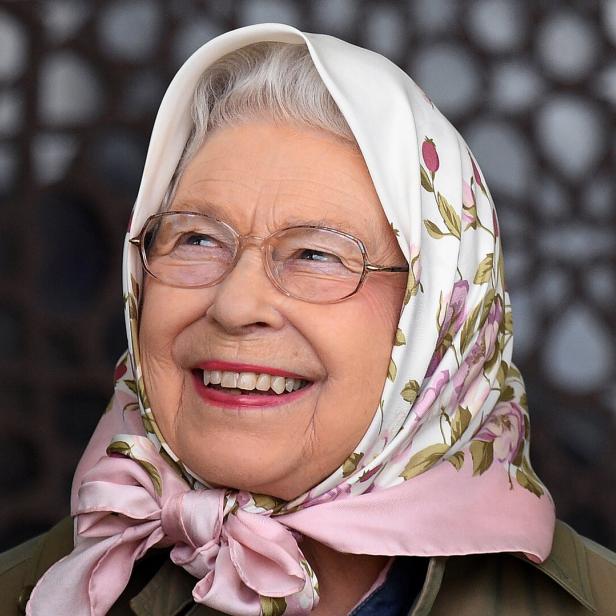 Eine lächelnde Queen Elizabeth mit Brille und einem geblümten Kopftuch schaut zur Seite.