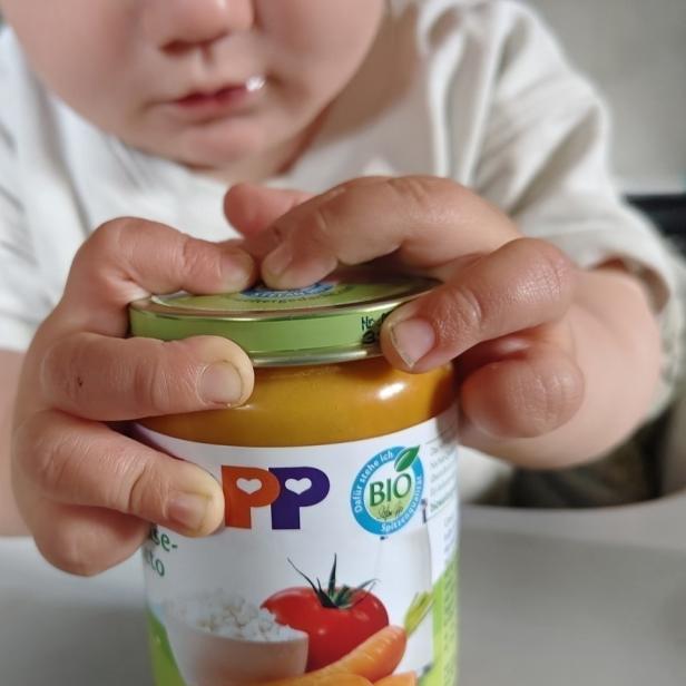 Ein Kleinkind versucht, ein Glas mit Babynahrung mit beiden Händen zu öffnen.