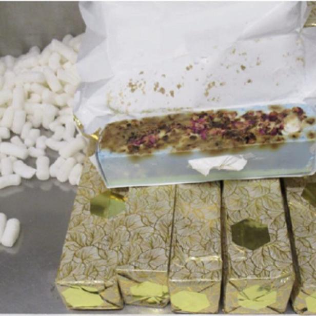 Eine offene Packung Seife mit Blüten liegt auf goldenen, blattgemusterten Schachteln, neben Verpackungschips.