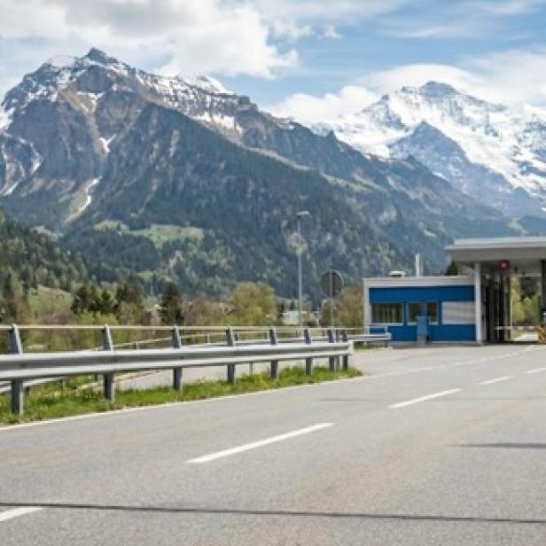 Eine Straße vor Bergen, rechts die Flagge der Schweiz 
