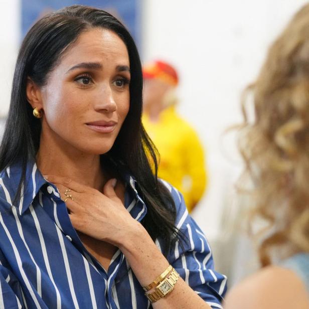 Meghan, in blau-weiß gestreifter Bluse und Goldschmuck, spricht mit einer Person.