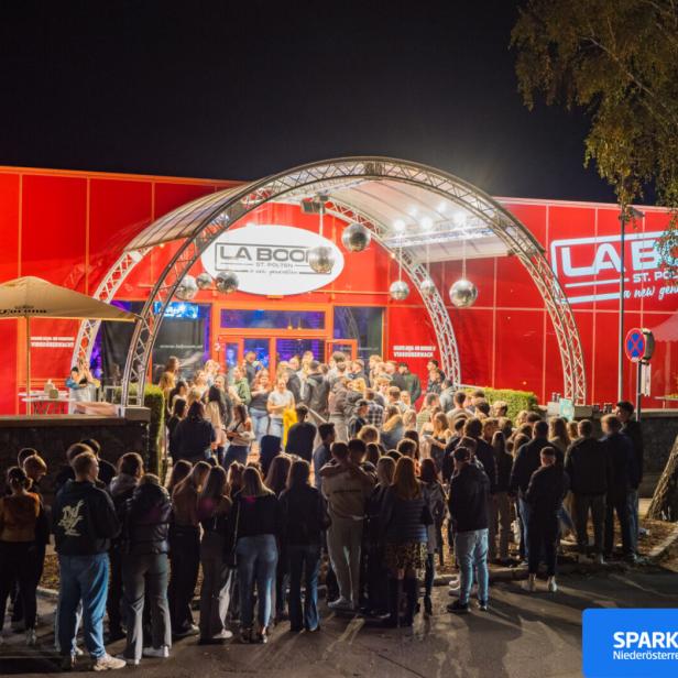 Viele Menschen stehen abends vor dem rot beleuchteten Eingang des Nachtclubs La Boom in St. Pölten.
