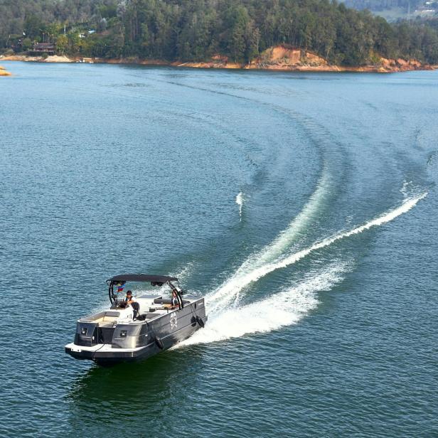 Motorboot fährt auf einem ruhigen See, im Hintergrund bewaldetes Ufer.