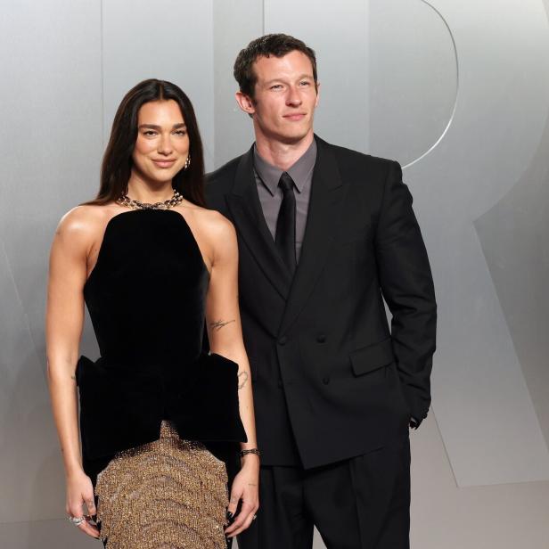 Dua Lipa und Callum Turner posieren vor einem silbernen Hintergrund.