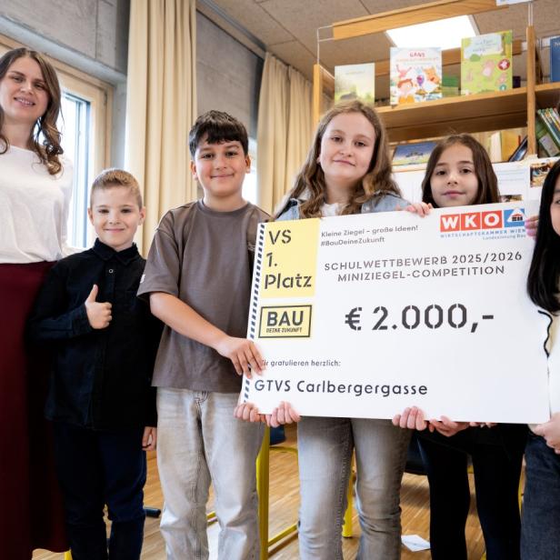 Kindergruppe mit Lehrerin hält Siegerscheck der Miniziegel-Competition in einem Klassenraum.