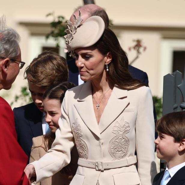 Prinzessin Kate, mit Hut und Kindern, schüttelt einem Mann in roter Robe die Hand.