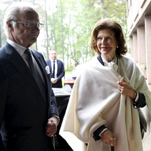 König Carl Gustaf und Königin Silvia von Schweden stehen draußen vor einem Gebäude.
