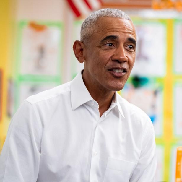 Barack Obama lächelt in einem hellen Raum mit Kinderzeichnungen im Hintergrund.