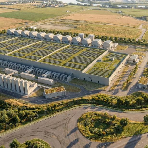 Großer Industriekomplex mit begrünten Dächern, umgeben von Feldern, Straßen und vereinzelten Bäumen.